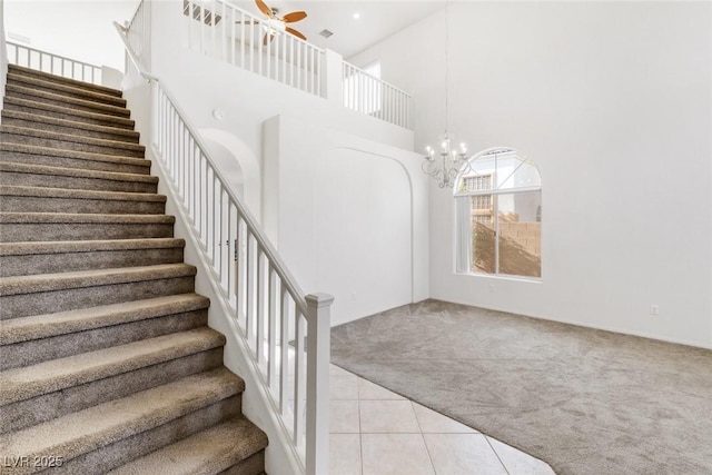 stairway with tile patterned flooring, ceiling fan with notable chandelier, and a high ceiling