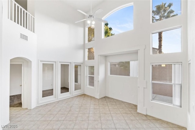 unfurnished living room with ceiling fan, a towering ceiling, a healthy amount of sunlight, and light tile patterned floors