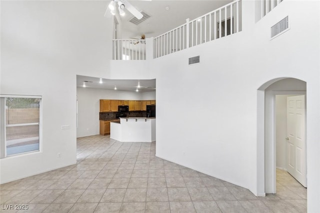 unfurnished living room with ceiling fan, light tile patterned flooring, and a high ceiling