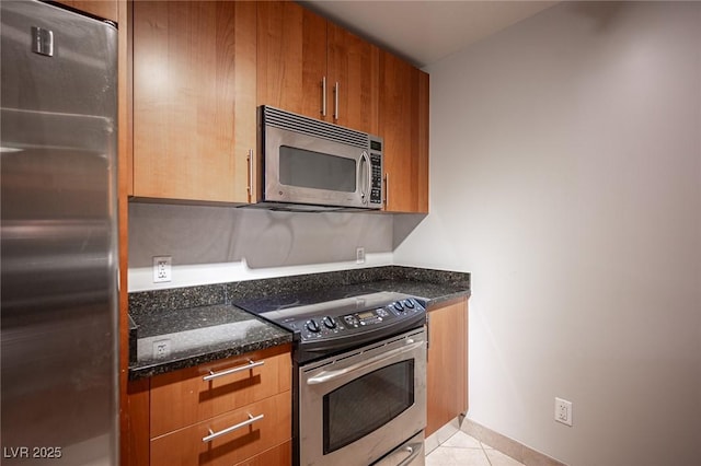 kitchen with light tile patterned floors, dark stone counters, and appliances with stainless steel finishes