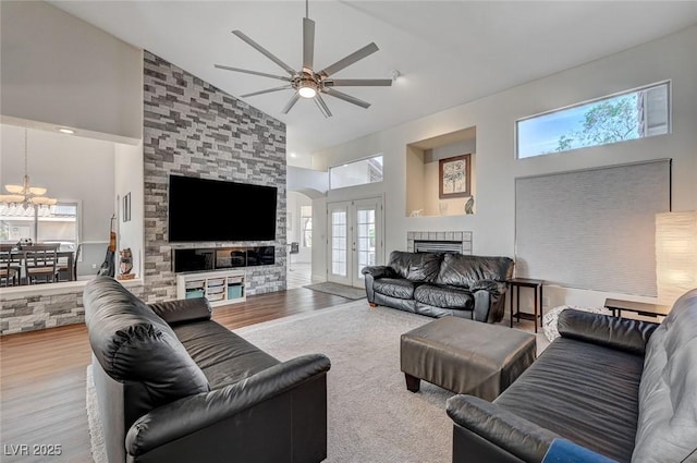 living room with high vaulted ceiling, french doors, ceiling fan with notable chandelier, light wood-type flooring, and a fireplace