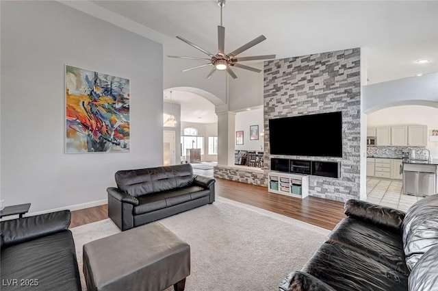 living room with light wood-type flooring, decorative columns, ceiling fan, sink, and high vaulted ceiling