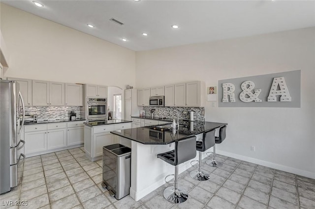 kitchen featuring a high ceiling, kitchen peninsula, dark stone countertops, a kitchen bar, and appliances with stainless steel finishes