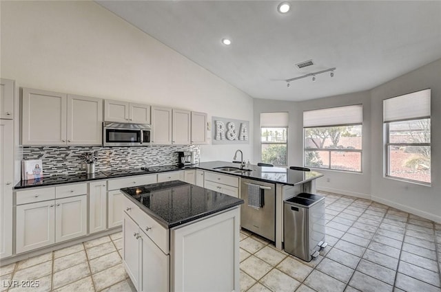 kitchen featuring rail lighting, stainless steel appliances, kitchen peninsula, dark stone countertops, and lofted ceiling