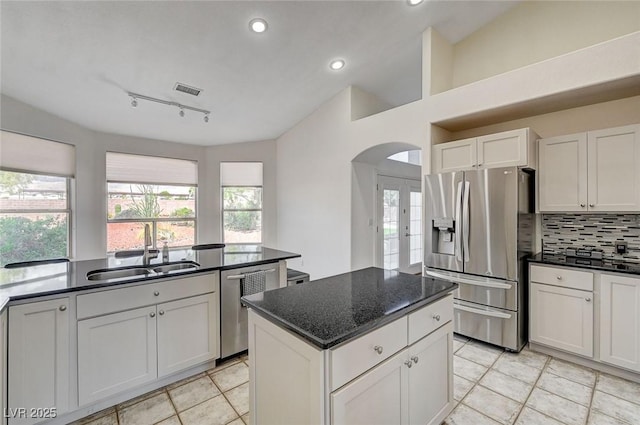 kitchen with appliances with stainless steel finishes, rail lighting, sink, white cabinets, and lofted ceiling