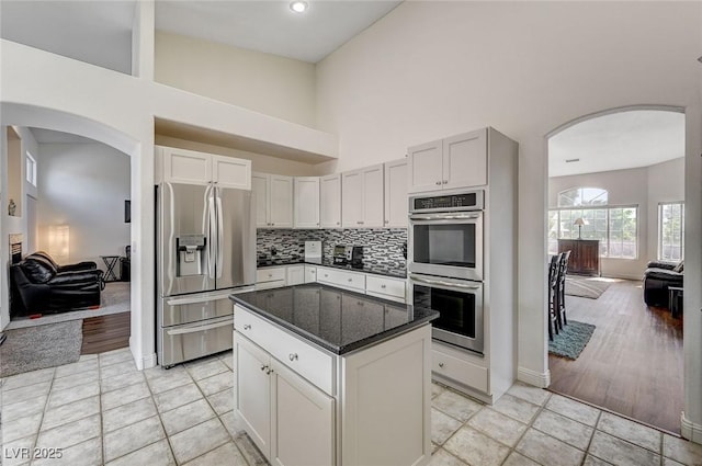 kitchen with backsplash, dark stone counters, stainless steel appliances, white cabinets, and a center island