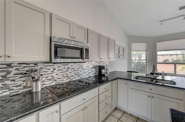 kitchen featuring dark stone counters, track lighting, black electric stovetop, sink, and light tile patterned floors