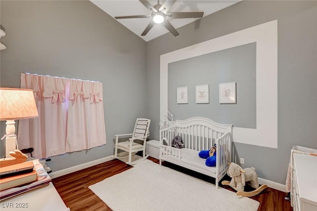 bedroom with vaulted ceiling, a nursery area, dark wood-type flooring, and ceiling fan