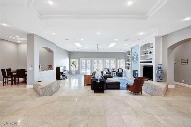 living room with a tray ceiling, built in features, ceiling fan, and ornamental molding