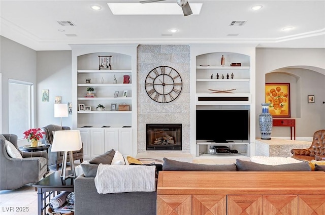 living room with built in shelves, ceiling fan, and a tile fireplace