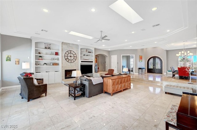 living room with built in shelves, ceiling fan with notable chandelier, a tile fireplace, and french doors