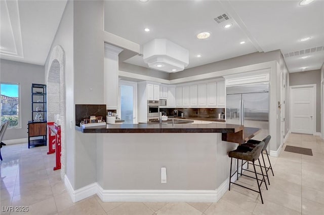 kitchen with kitchen peninsula, tasteful backsplash, white cabinetry, and a breakfast bar area