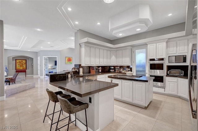 kitchen with white cabinetry, sink, double oven, kitchen peninsula, and a breakfast bar