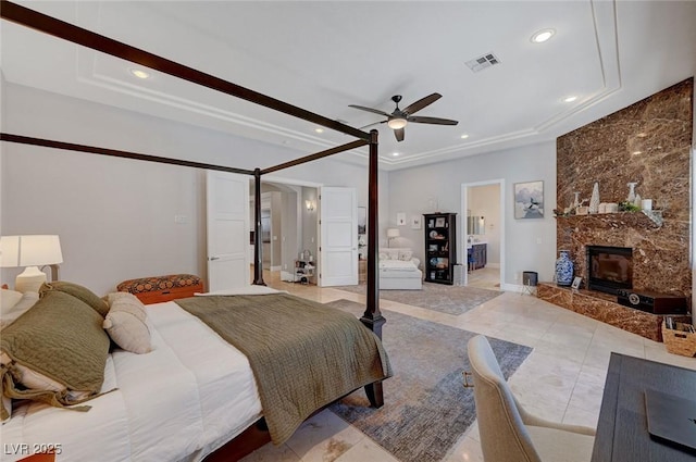 bedroom featuring a fireplace, connected bathroom, a tray ceiling, and ceiling fan