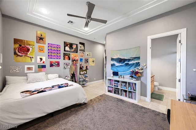 tiled bedroom with ceiling fan, a tray ceiling, and ensuite bath