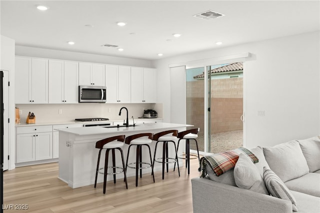 kitchen featuring a kitchen island with sink, sink, light hardwood / wood-style flooring, white cabinetry, and a breakfast bar area