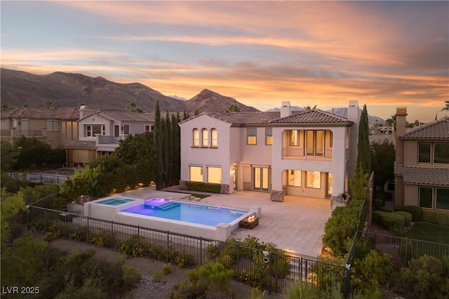 back house at dusk featuring a patio area, an in ground hot tub, and a mountain view