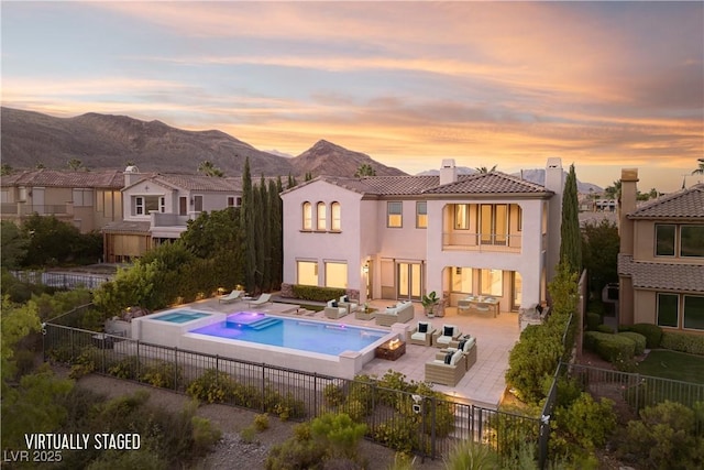 back house at dusk with outdoor lounge area, a mountain view, a patio area, and an in ground hot tub