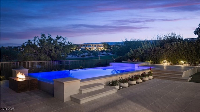 pool at dusk with a patio area and an outdoor fire pit