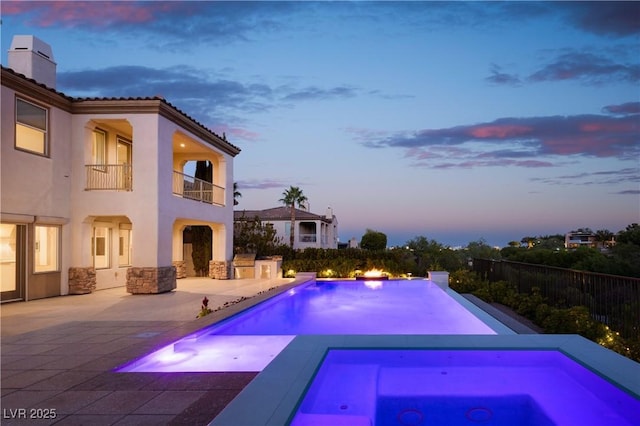 pool at dusk with a patio area and an in ground hot tub