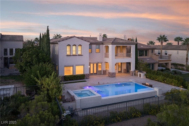 back house at dusk featuring a balcony, a patio area, and a pool with hot tub