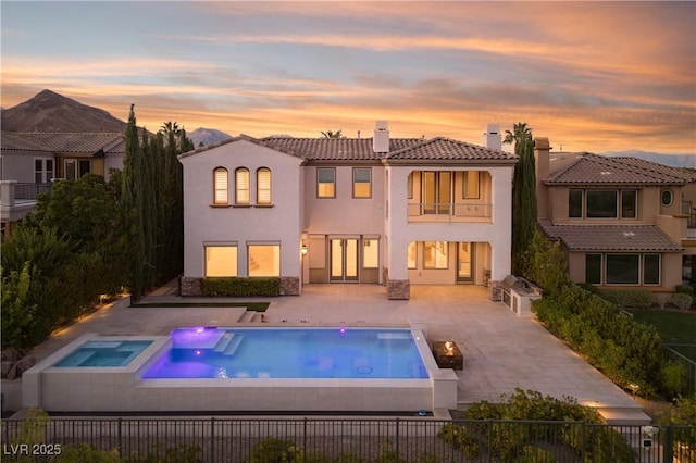 back house at dusk with a patio and a pool with hot tub