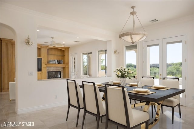 dining area with ceiling fan, crown molding, a fireplace, and french doors