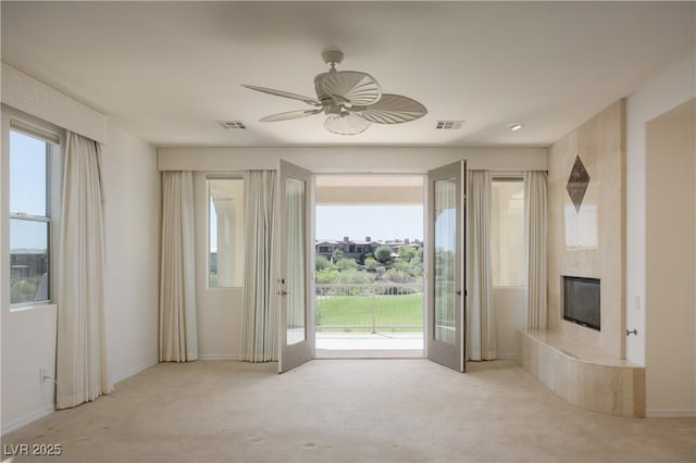 unfurnished living room with a tiled fireplace, ceiling fan, plenty of natural light, and light colored carpet