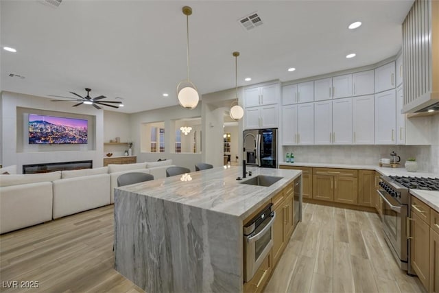 kitchen featuring an island with sink, decorative light fixtures, light stone counters, white cabinetry, and stainless steel appliances