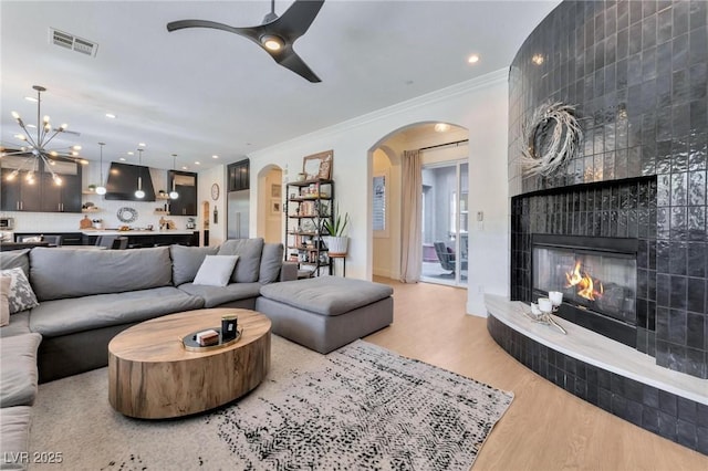 living room featuring hardwood / wood-style flooring, ceiling fan with notable chandelier, crown molding, and a fireplace