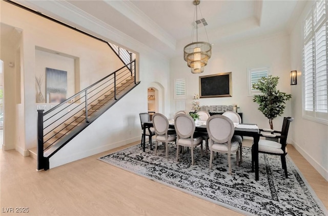 dining room featuring an inviting chandelier, a tray ceiling, light hardwood / wood-style flooring, and a healthy amount of sunlight