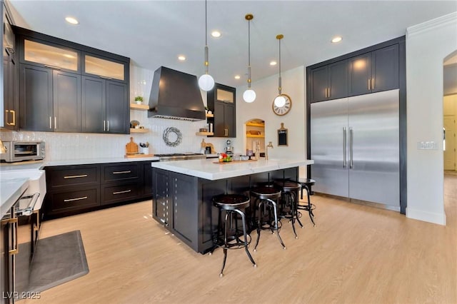 kitchen with a breakfast bar, wall chimney range hood, hanging light fixtures, appliances with stainless steel finishes, and a kitchen island