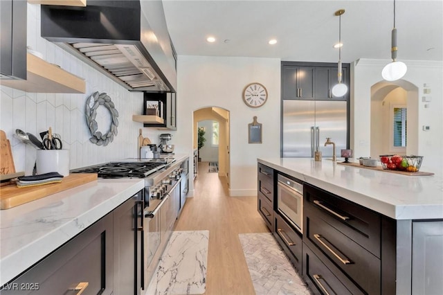 kitchen with light stone countertops, hanging light fixtures, tasteful backsplash, built in appliances, and extractor fan