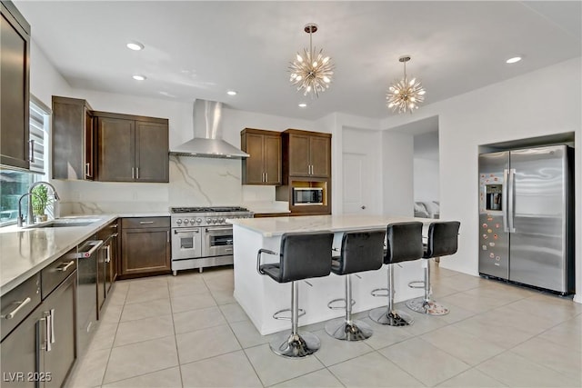 kitchen featuring a center island, hanging light fixtures, stainless steel appliances, wall chimney range hood, and an inviting chandelier