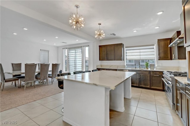 kitchen featuring light colored carpet, decorative light fixtures, stainless steel stove, a kitchen island, and plenty of natural light