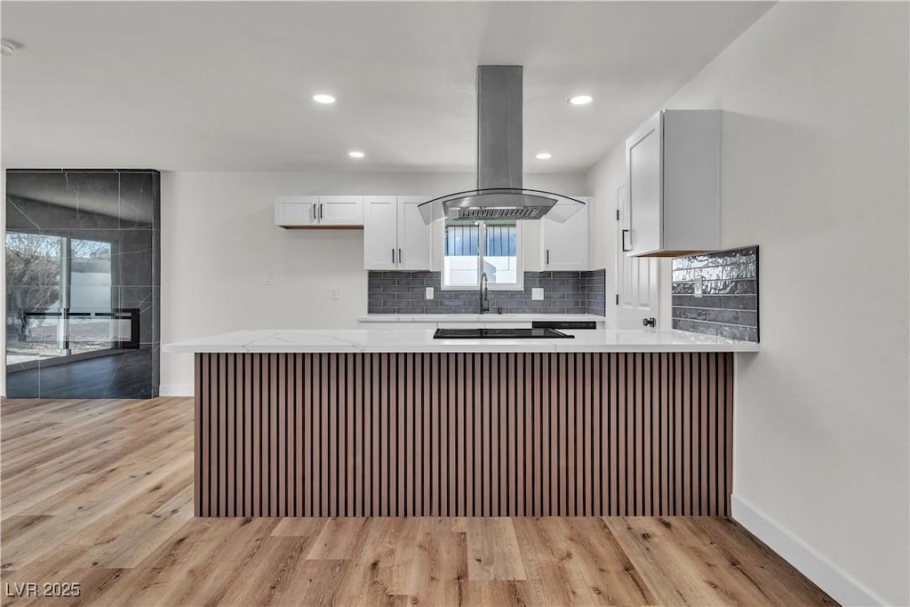 kitchen with kitchen peninsula, backsplash, island range hood, white cabinets, and light hardwood / wood-style floors