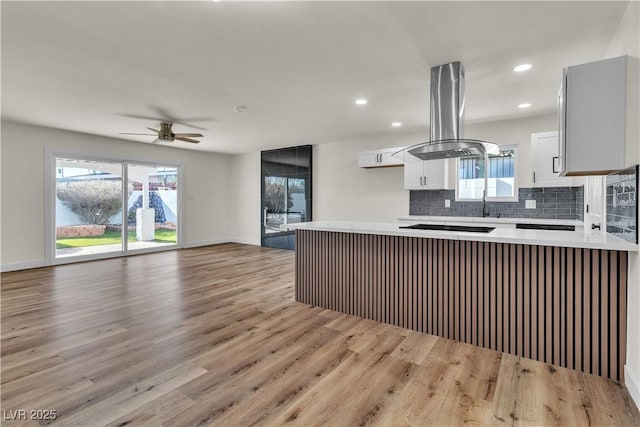 kitchen with tasteful backsplash, light hardwood / wood-style floors, black electric cooktop, island range hood, and white cabinets