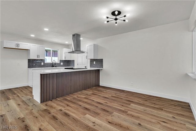 kitchen with kitchen peninsula, light wood-type flooring, island range hood, sink, and white cabinets