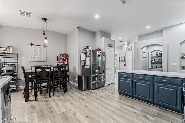 kitchen featuring hanging light fixtures, a barn door, stainless steel fridge with ice dispenser, light hardwood / wood-style flooring, and blue cabinets