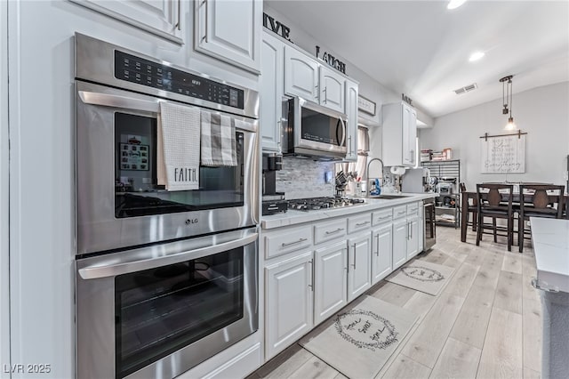 kitchen with appliances with stainless steel finishes, tasteful backsplash, sink, pendant lighting, and white cabinets