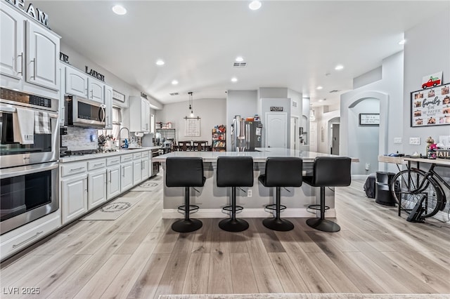 kitchen featuring pendant lighting, a breakfast bar, a kitchen island, white cabinetry, and stainless steel appliances