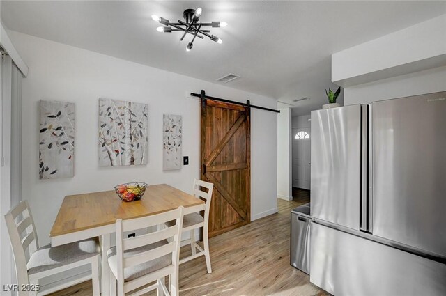 dining area with a barn door, light wood-type flooring, and an inviting chandelier