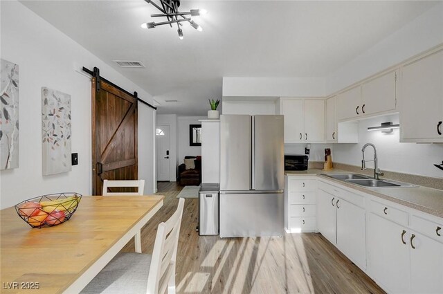 kitchen with a barn door, sink, stainless steel refrigerator, and white cabinetry