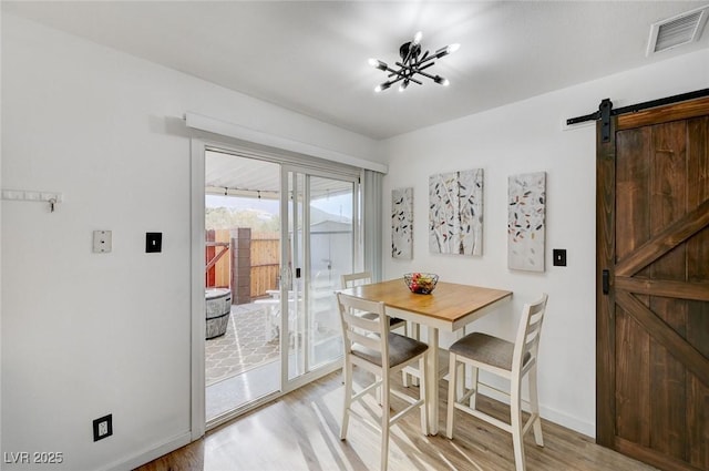 dining room featuring an inviting chandelier, a barn door, and light hardwood / wood-style flooring