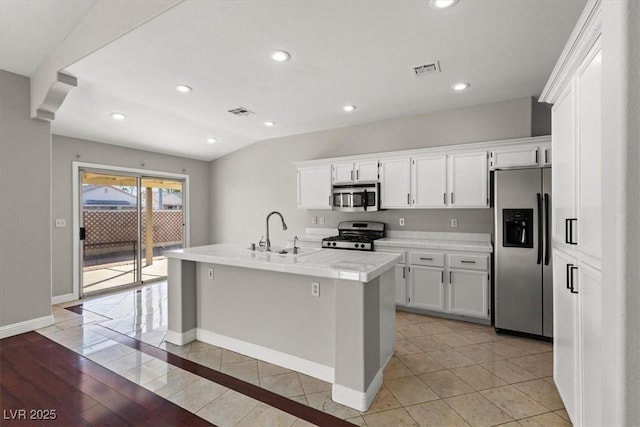 kitchen with sink, an island with sink, vaulted ceiling, white cabinets, and appliances with stainless steel finishes