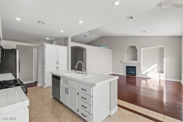 kitchen featuring a center island with sink, tile counters, white cabinetry, and appliances with stainless steel finishes