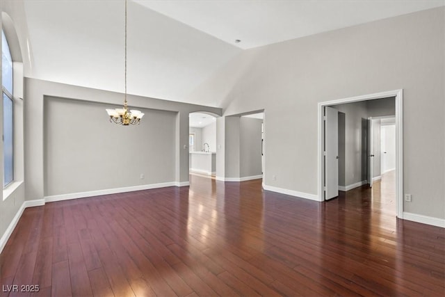 unfurnished room featuring high vaulted ceiling, dark wood-type flooring, and an inviting chandelier