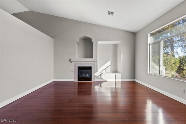 unfurnished living room with dark hardwood / wood-style floors, lofted ceiling, and a tiled fireplace