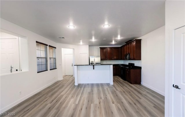 kitchen with stainless steel fridge, a center island with sink, dark brown cabinets, and light hardwood / wood-style floors