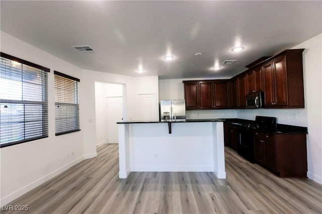 kitchen with dark brown cabinetry, a kitchen island with sink, light hardwood / wood-style flooring, and appliances with stainless steel finishes